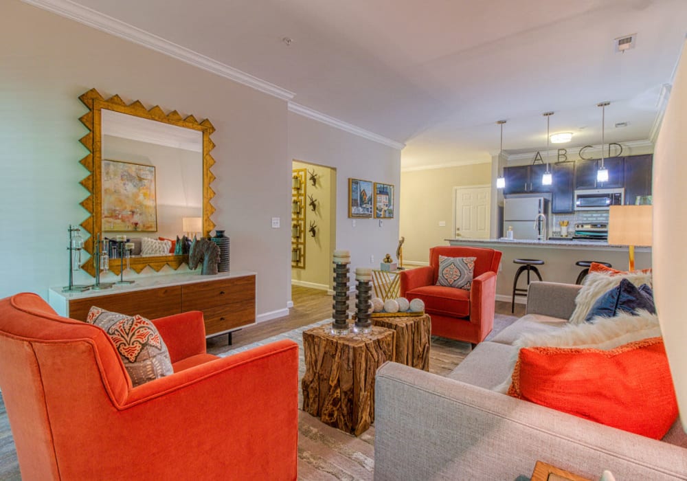 Open layout living room and connecting kitchen vibrantly decorated with orange chairs, white couch, and coffee table at Greymont Village in Asheville, North Carolina