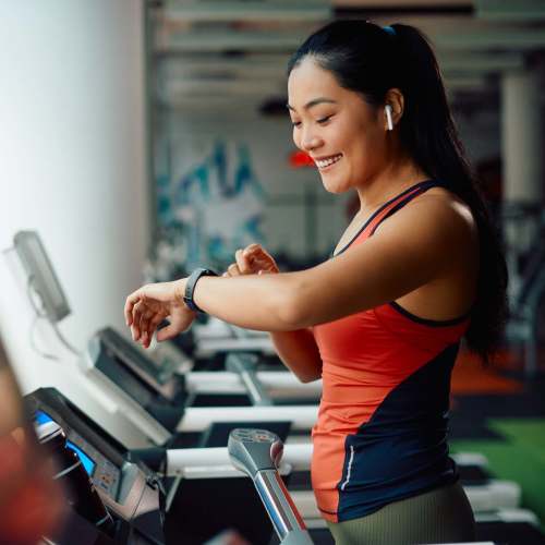 Woman smiling while checking fitness watch at gym treadmill at Creekside At Legacy in Plano, Texas