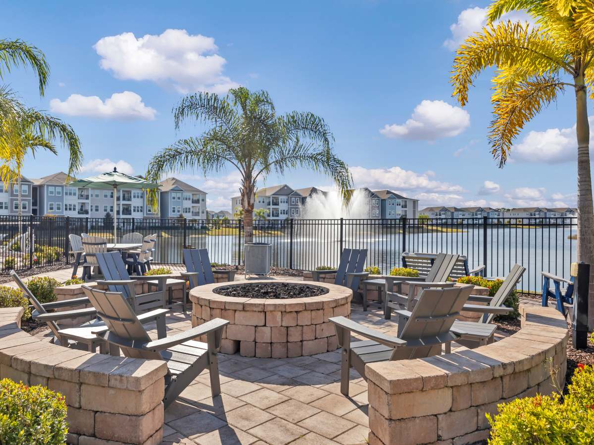 Resort-style fire pit area with seating overlooking a tranquil lake and fountain at The Carlton of West Melbourne in West Melbourne, Florida