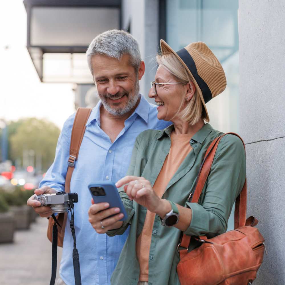 Couple enjoying time together, looking at a smartphone, smiling, holding a camera at Lindbergh Parc Senior Apartments in Fort Worth, Texas