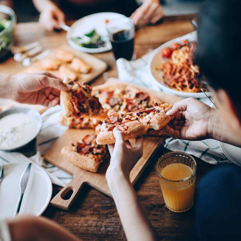 Hands reaching for pizza slices at Avia Lofts at Maple Road in Amherst, New York