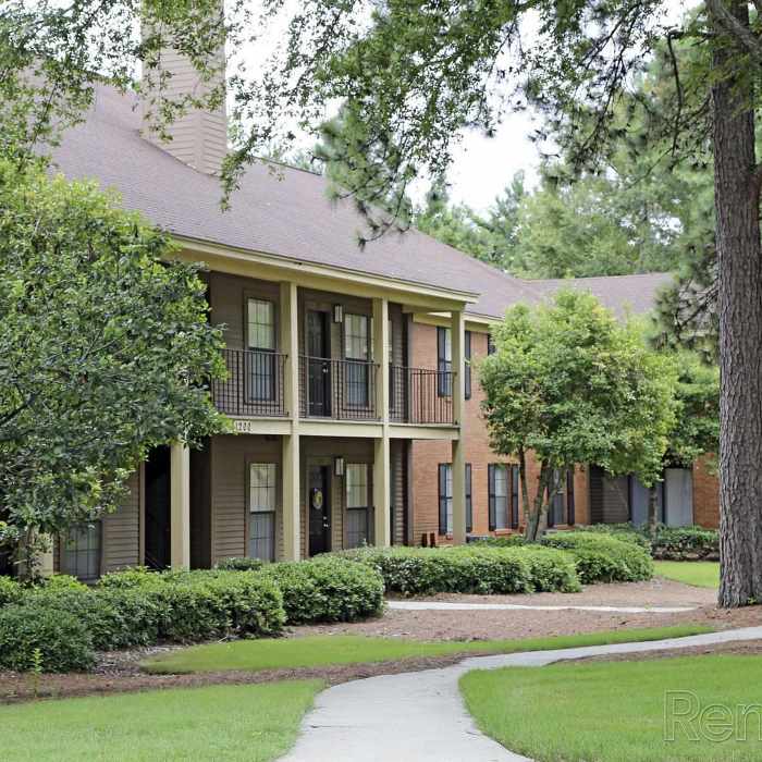 Two-story apartment buildings with balconies surrounded by lush landscaping and a winding path at Stevens Creek Commons in Augusta, Georgia