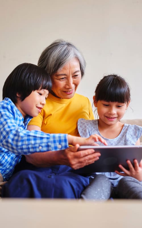 An elderly woman with two kids reading a book together at The Pillars of Lakeville in Lakeville, Minnesota