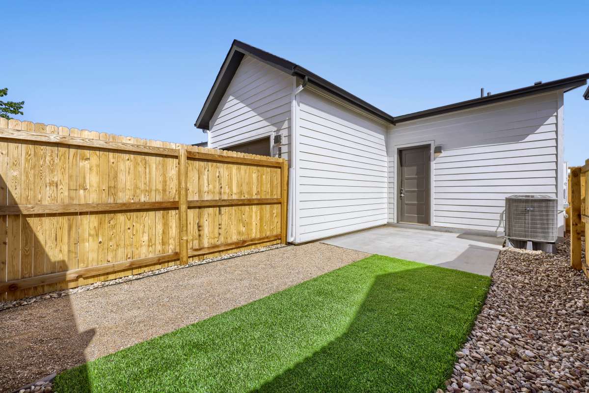 Exterior photo of rental home fenced in backyard with turf, rock, and cement pad
