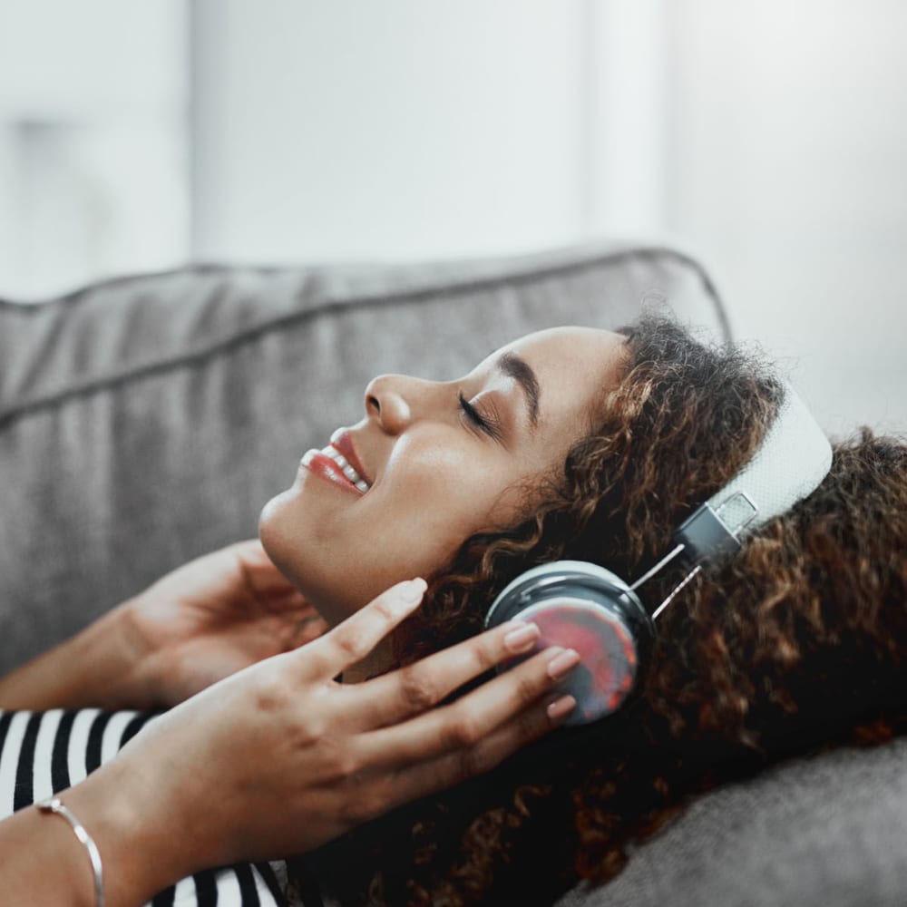 Resident relaxing on the couch and listening to music on headphones in her home at Oaks Braemar in Edina, Minnesota