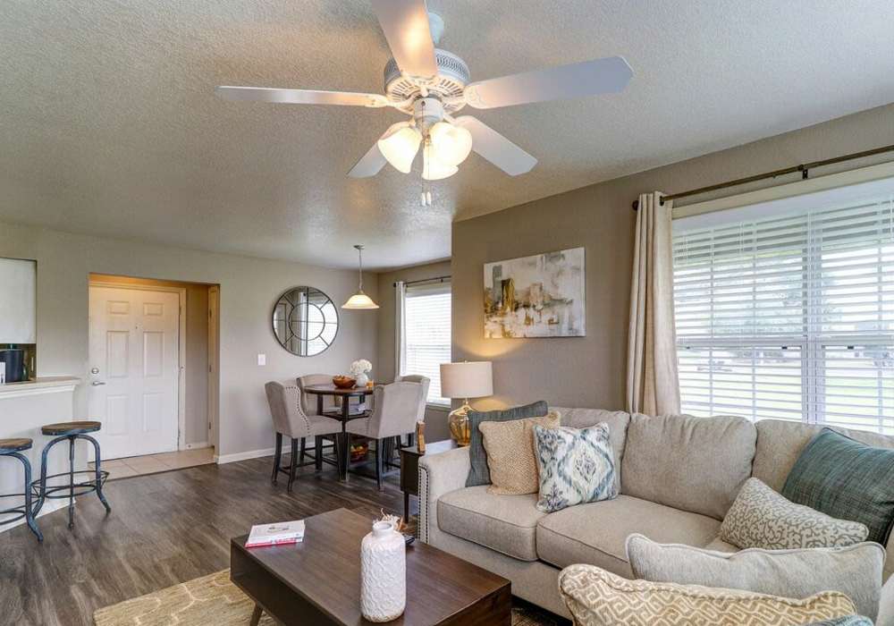 Modern living room with large couch, ceiling fan and wood-style flooring at The Reserve at Kanapaha in Gainesville, Florida