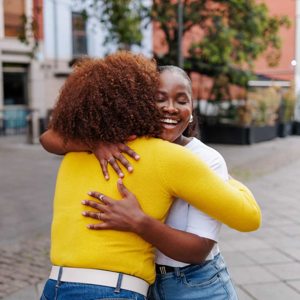 Two women embracing joyfully outdoors near The Simone in Silver Spring, Maryland