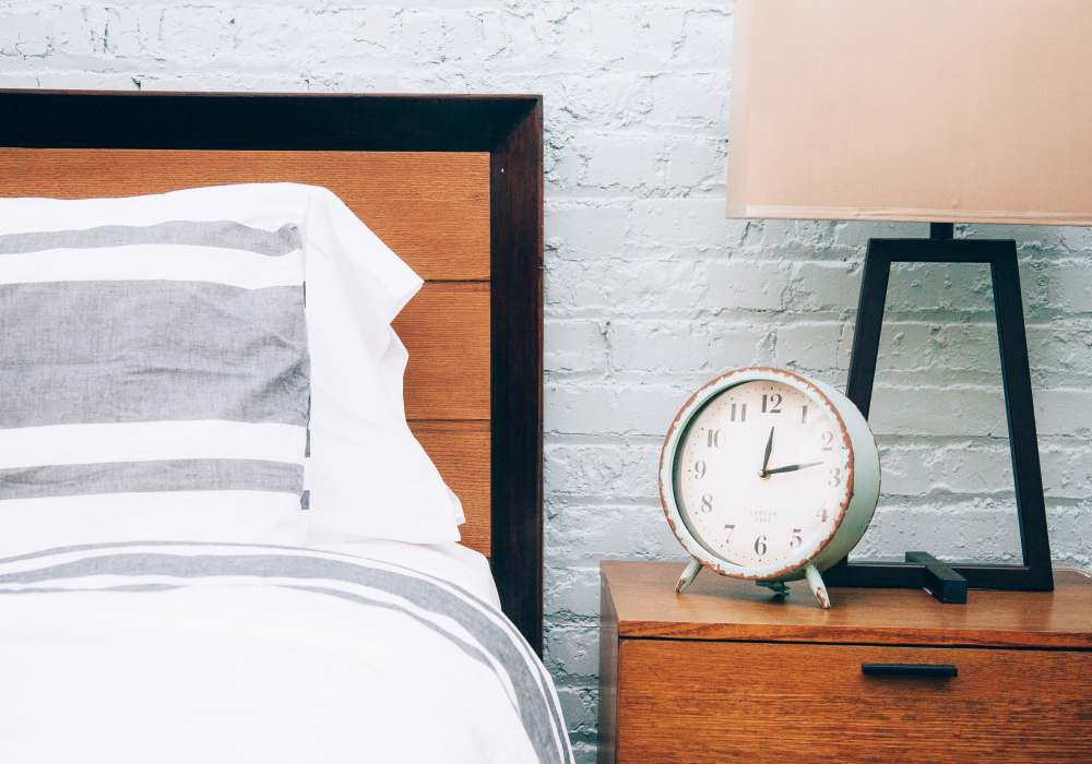 Bedroom nightstand with vintage clock, table lamp and wood headboard against exposed brick wall at City View Lofts in Richmond, Virginia