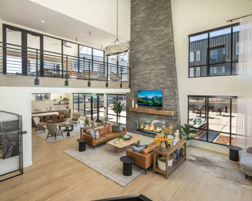 Clubhouse with resident seating area, TV, fireplace, chandelier light and large windows with view of outdoor lounge area at Clovis Point in Longmont, Colorado