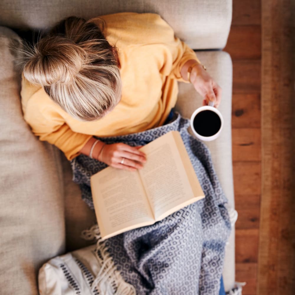 A resident relaxes on her sofa with a book and coffee a Highland Hills, Cumberland, Rhode Island