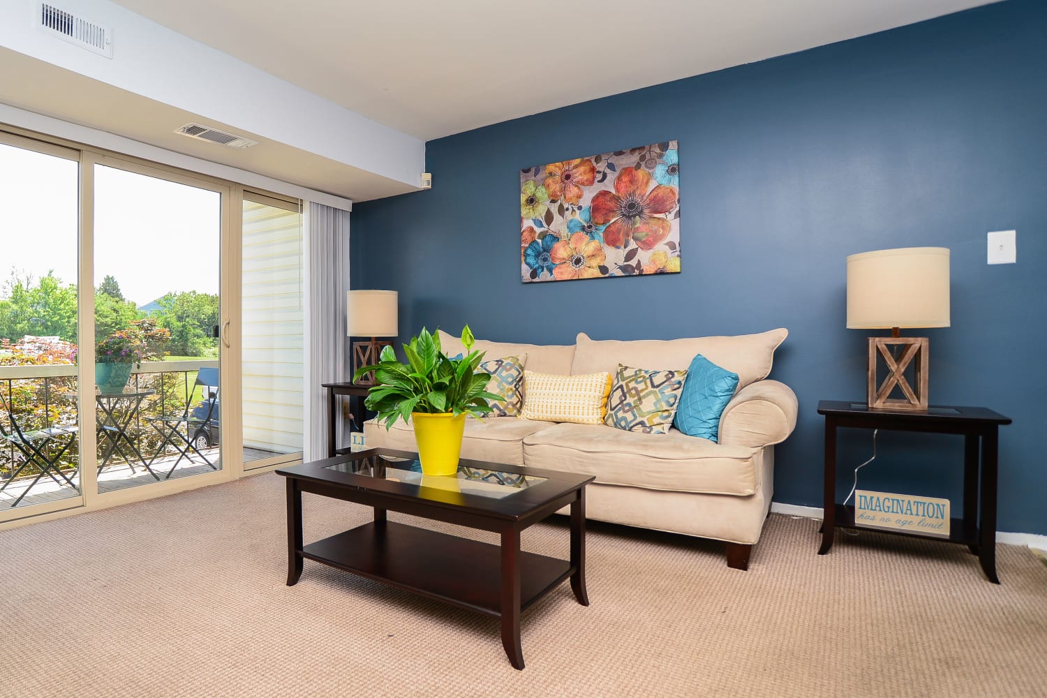 Model living room with plush carpeting and sliding door access to a private balcony at Ross Ridge Apartment Homes in Baltimore, Maryland