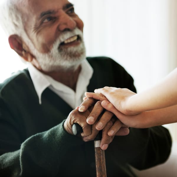 Resident resting their hands on a cane and looking up at a caretaker at a Living Care Lifestyles community