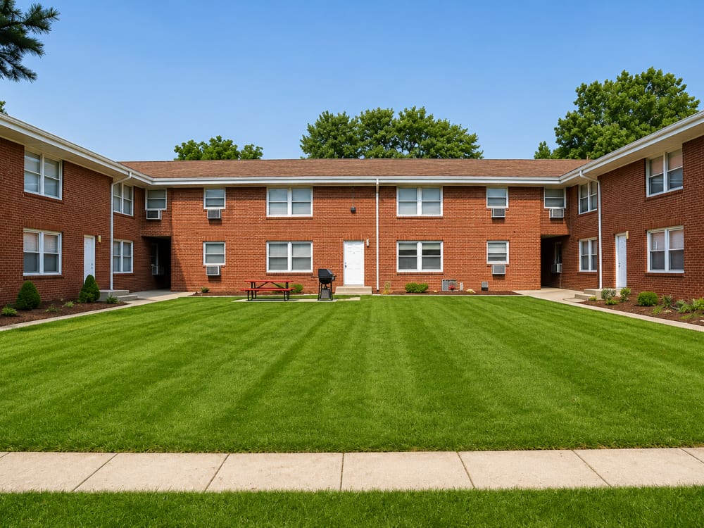 Brick apartment buildings with well-manicured lawn and picnic table in the courtyard at South Oak in Ames, Iowa