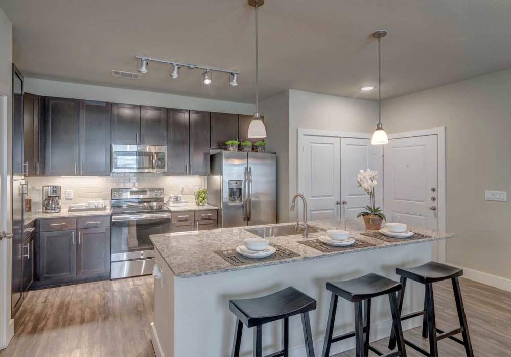 Kitchen with dark cabinets, granite island, bar stools and pendant lighting at Southfork Lake in Manvel, Texas