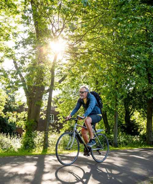 Man riding a bicycle on a tree-lined path in bright sunlight near Stevens Creek Commons in Augusta, Georgia