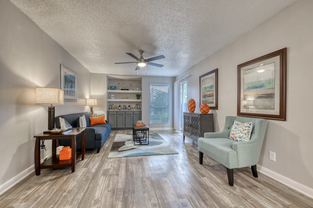 An apartment living area with wood-style flooring and a ceiling fan at Villas de Santa Fe in San Antonio, Texas