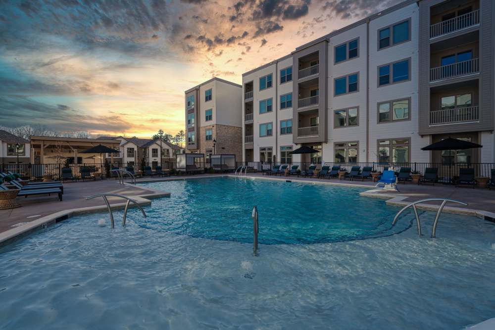 Resort-style swimming pool surrounded by lounge chairs and multi-story apartment buildings at sunset with dramatic cloud formations in the sky at The Reserve at Patterson Place in Durham, North Carolina.
