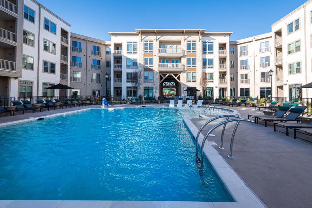 Large outdoor swimming pool surrounded by lounge chairs and apartment buildings under a clear blue sky at The Reserve at Patterson Place in Durham, North Carolina.