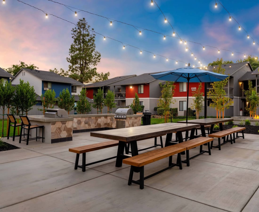 Two-BR Apartments in Dixon, CA - The Mews at Dixon Farms - Outdoor Grill Area with Two BBQs, Counter Space, Stools, Picnic Tables, Umbrella, and Cafe Lights. at  The Mews At Dixon Farms in Dixon, California