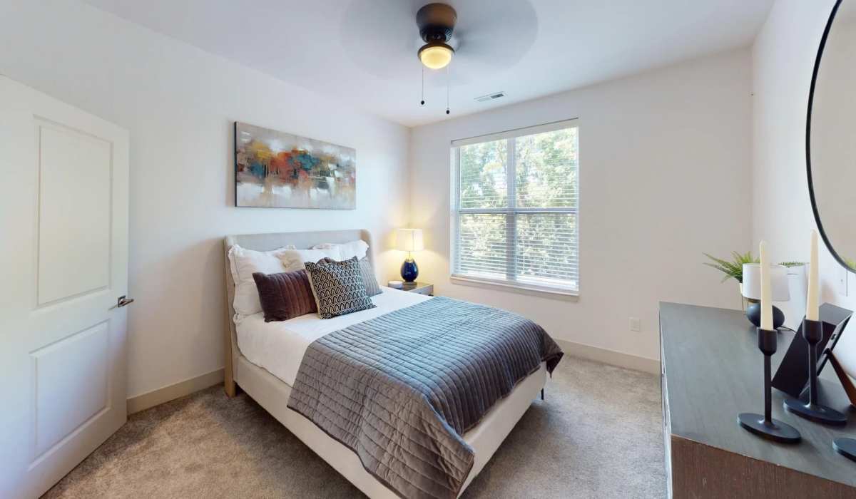 Modern bedroom inside the Altitude floor plan at Elevation 800, featuring a large window, ceiling fan, stylish décor, and plush carpeting in a bright, contemporary apartment home.