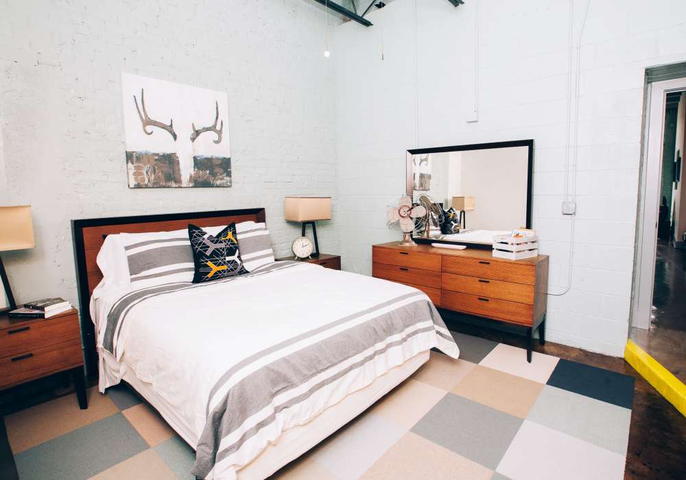 Bedroom with large bed, white bedding, nightstand and wall artwork at City View Lofts in Richmond, Virginia