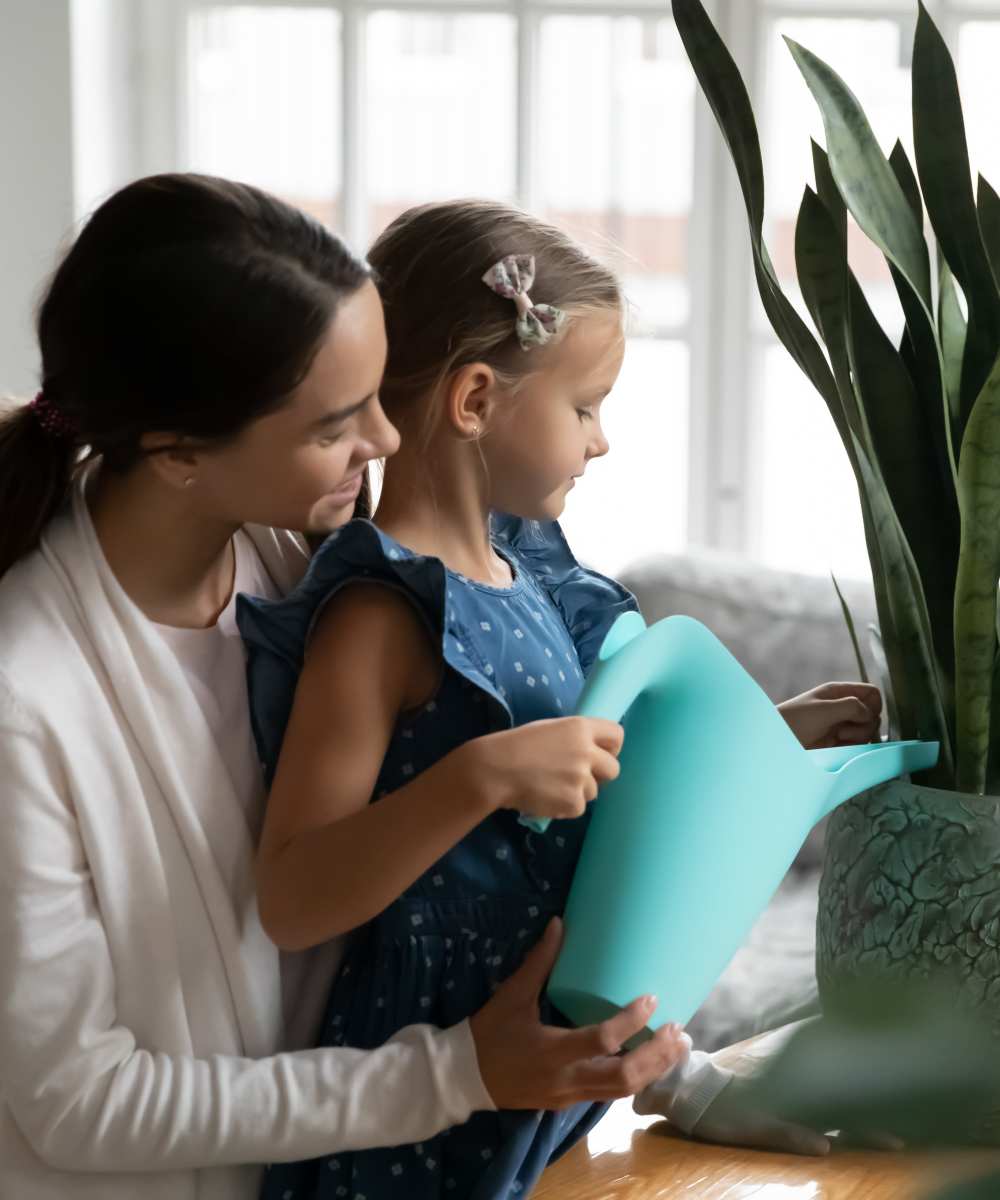 Women and daughter watering a plant in living room at Stonecrest Apartments in Spokane, Washington