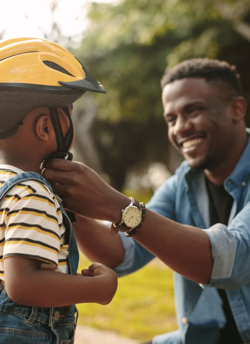 A dad putting a bike helmet on his son at Marquis Ellis Crossing in Durham, North Carolina