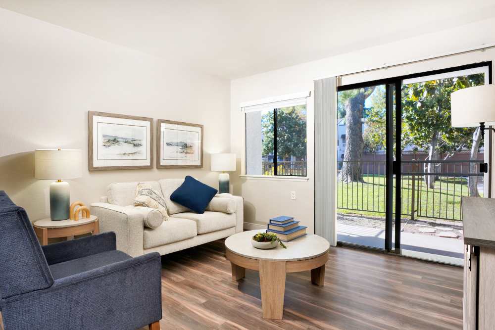 Bright living room with modern furniture, wood-style flooring, and sliding glass doors leading to a grassy outdoor area at Citrus Place in Riverside, California