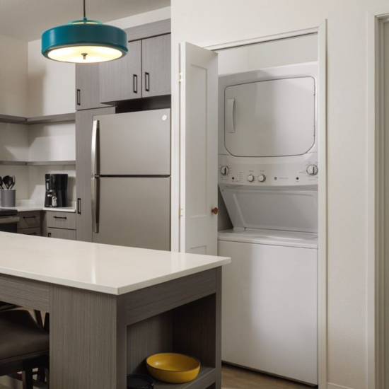 Kitchen with island, stainless steel refrigerator, modern appliances, and in-unit washer and dryer at Waterwalk Tucson in Tucson, Arizona