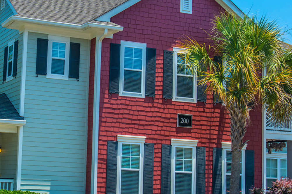 Two-story apartment house with red siding and white trim with a welcoming porch. Palm trees and lush greenery at Magnolia Downs in Charleston, South Carolina