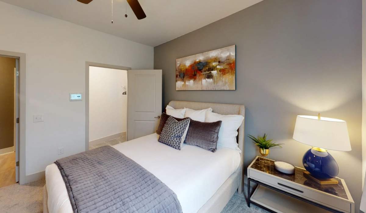 Modern bedroom in the Apex floor plan at Elevation 800 featuring a gray accent wall, contemporary artwork, upholstered bed, and stylish nightstand lighting