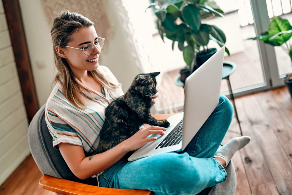 Resident working on a laptop with her cat on her lap in their apartment home at Oaks Trinity in Dallas, Texas