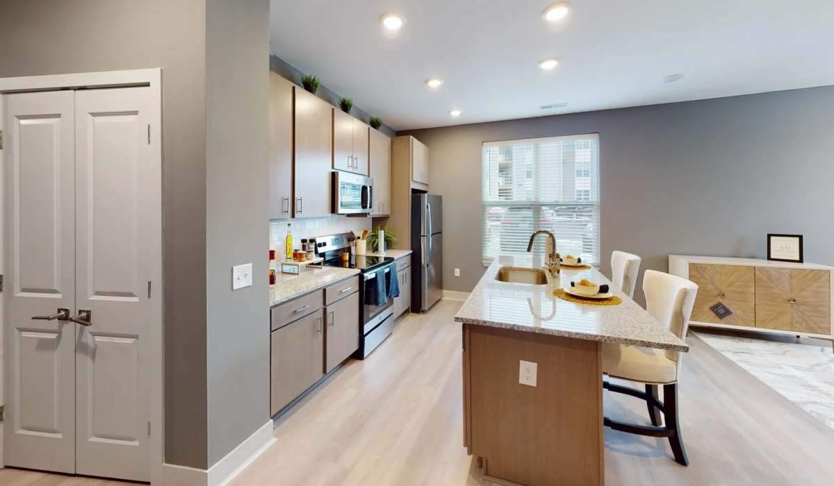 Spacious Apex floor plan kitchen at Elevation 800 featuring a large island with seating, stainless steel appliances, granite countertops, and modern light wood cabinetry.