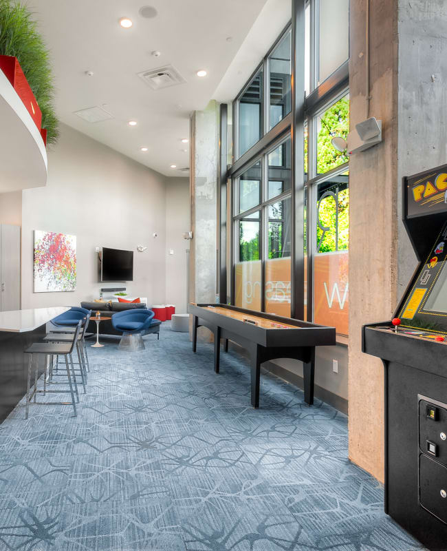 common area clubhouse lounge with couches, tv, shuffleboard, pac-man game, and kitchen at Tria Apartments in Newcastle