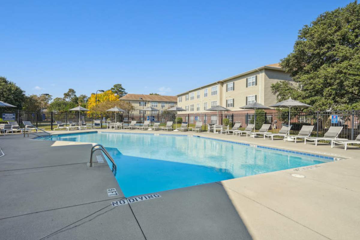 Swimming pool with patio and beach chairs on the side at Woodland Crossing Apartment Homes in New Bern, North Carolina