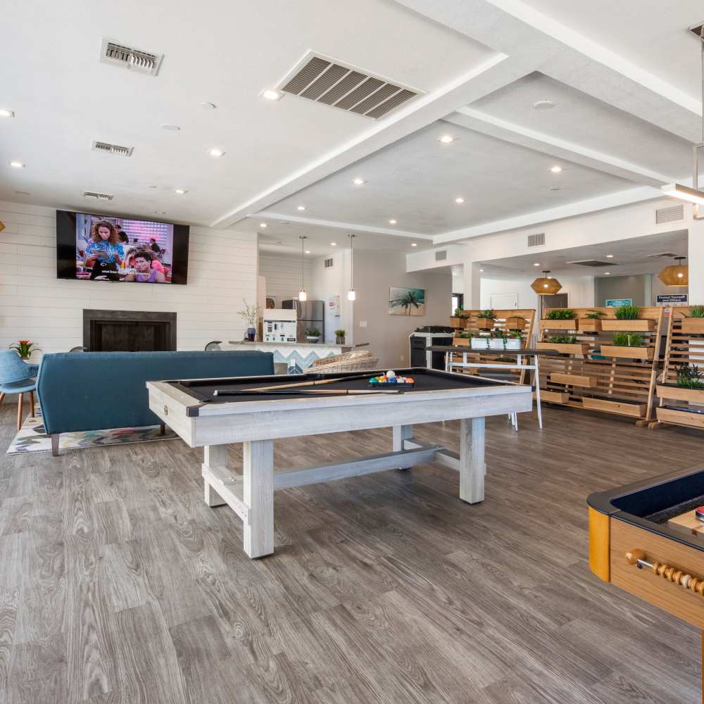 Modern community lounge with wood-style flooring, pool table, and large TV above a fireplace at Fairways on Thunderbird in Phoenix, Arizona