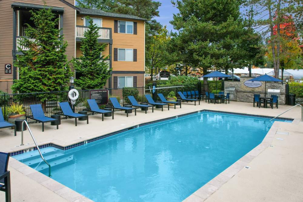 Sparking pool view with lounge chairs, tables and umbrellas at Newport Crossing Apartments in Newcastle, Washington
