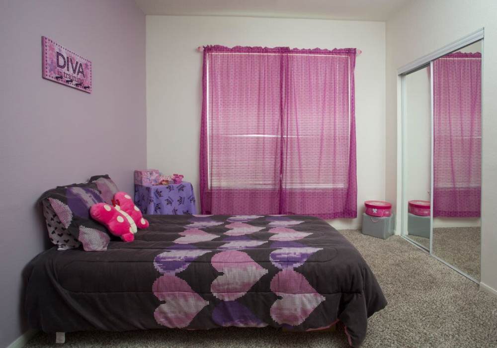 Cozy bedroom with purple walls, patterned bedding, and large mirror wardrobe at Las Palmas Apartments in Brownsville, Texas