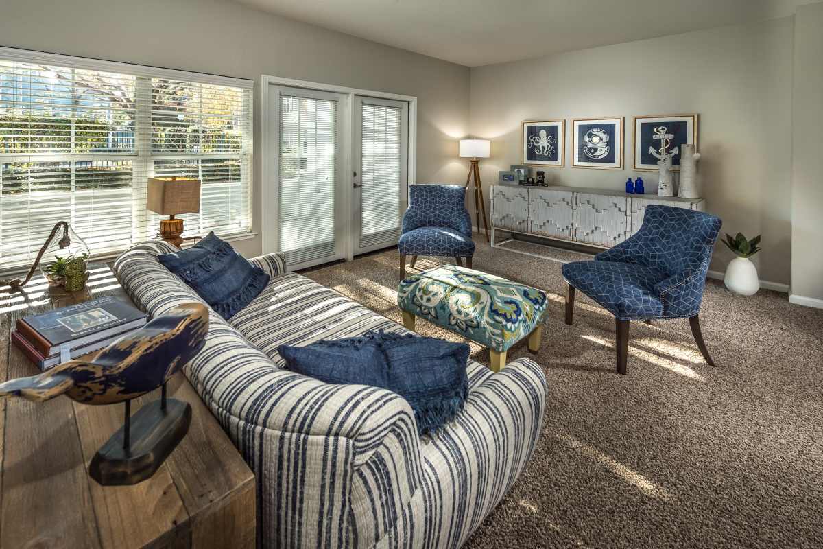 Spacious living room with large couch, chairs and large windows at Nantucket Apartments in Santa Clara, California