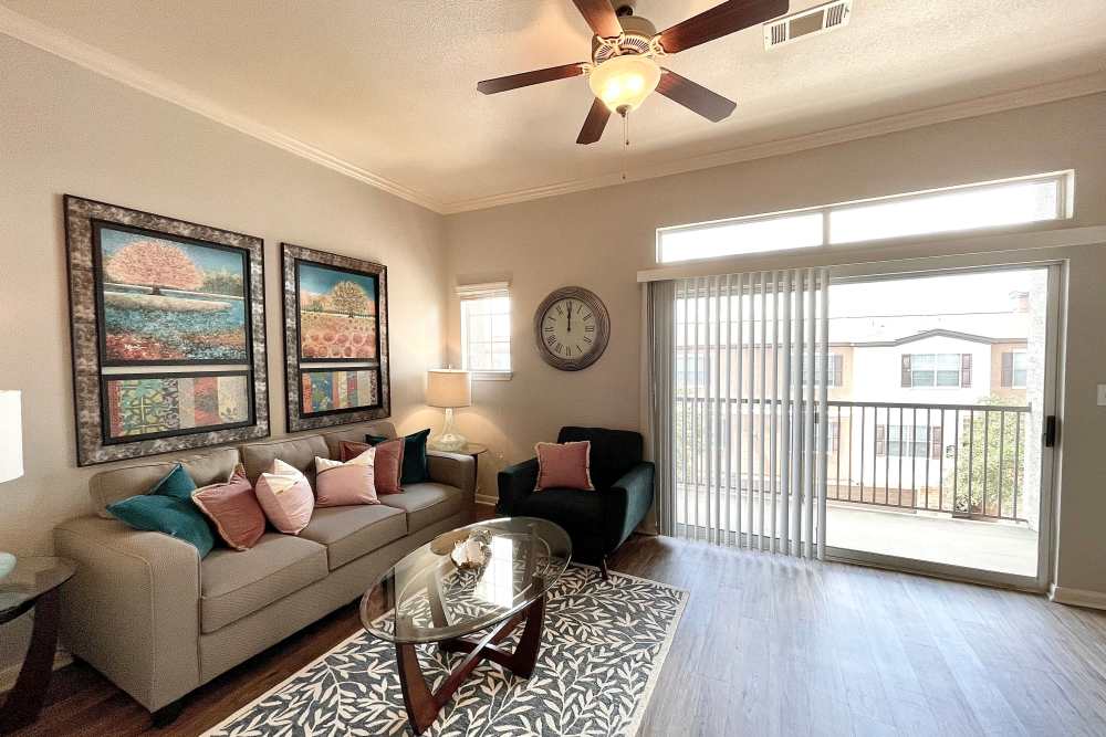 Spacious living room with large sofa, glass coffee table, ceiling fan and access to private patio at The Abbey at Stone Oak in San Antonio, Texas