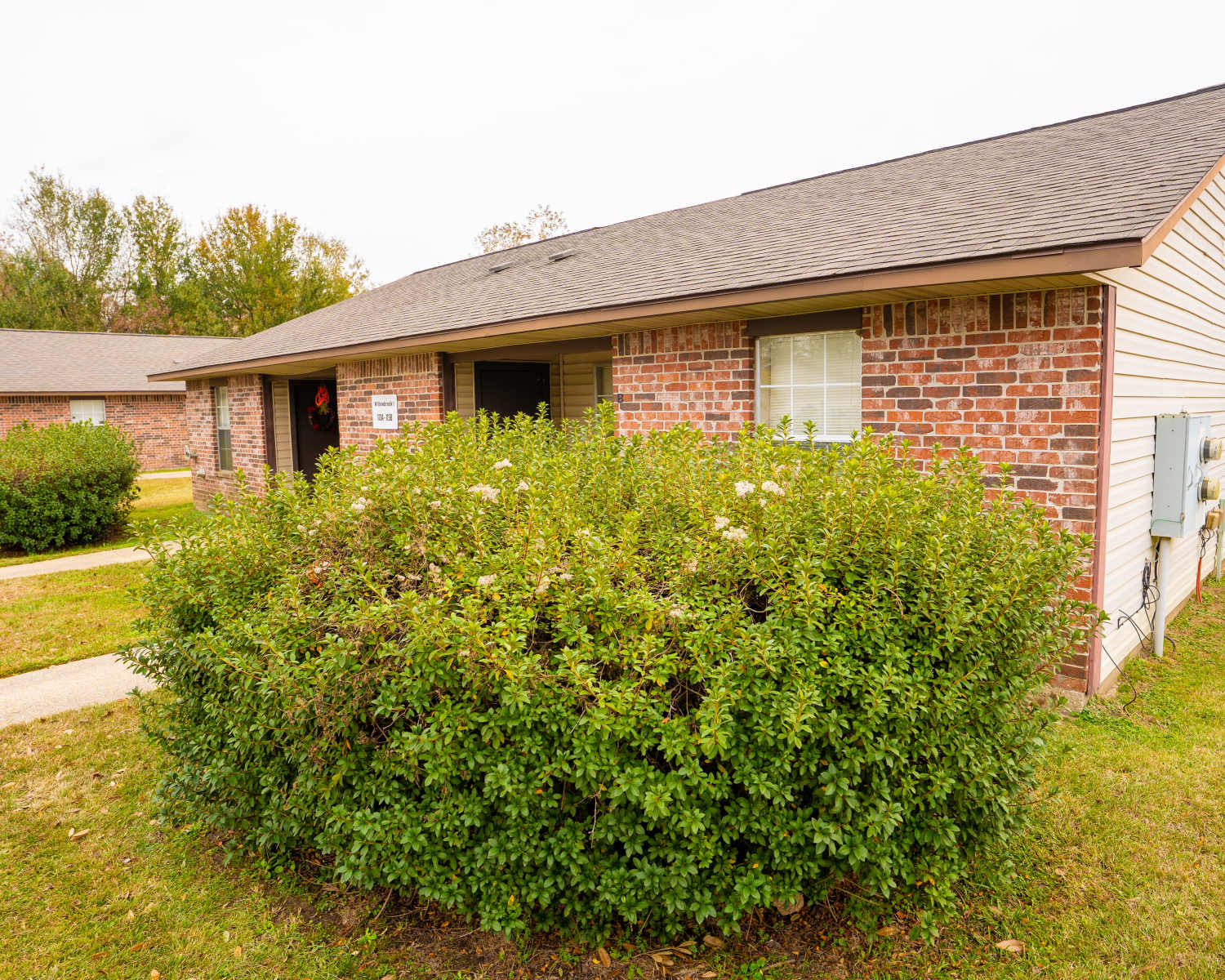 Brick apartment building with landscaped bushes and a clear pathway to the entrance at Willowbrook I in Lafayette, Louisiana