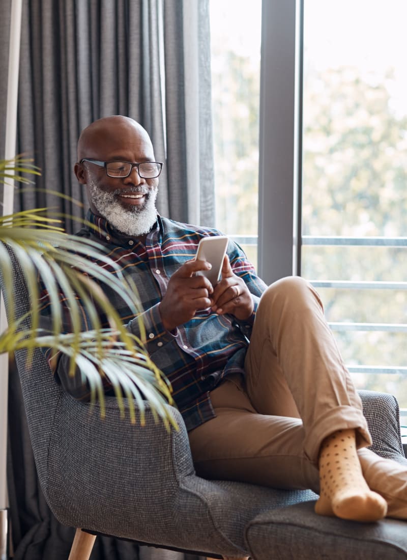 Resident relaxing in comfy chair with smartphone at Marquis at Carmel Commons in Charlotte, North Carolina