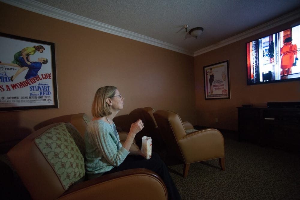 A resident watching a movie in the theater room at The Ridge at Oregon City in Oregon City, Oregon