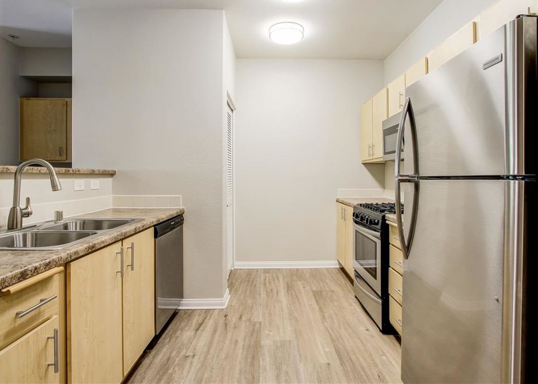 Modern kitchen with light wood cabinetry and hardwood flooring in a model home at Sierra Oaks Apartments in Turlock, California