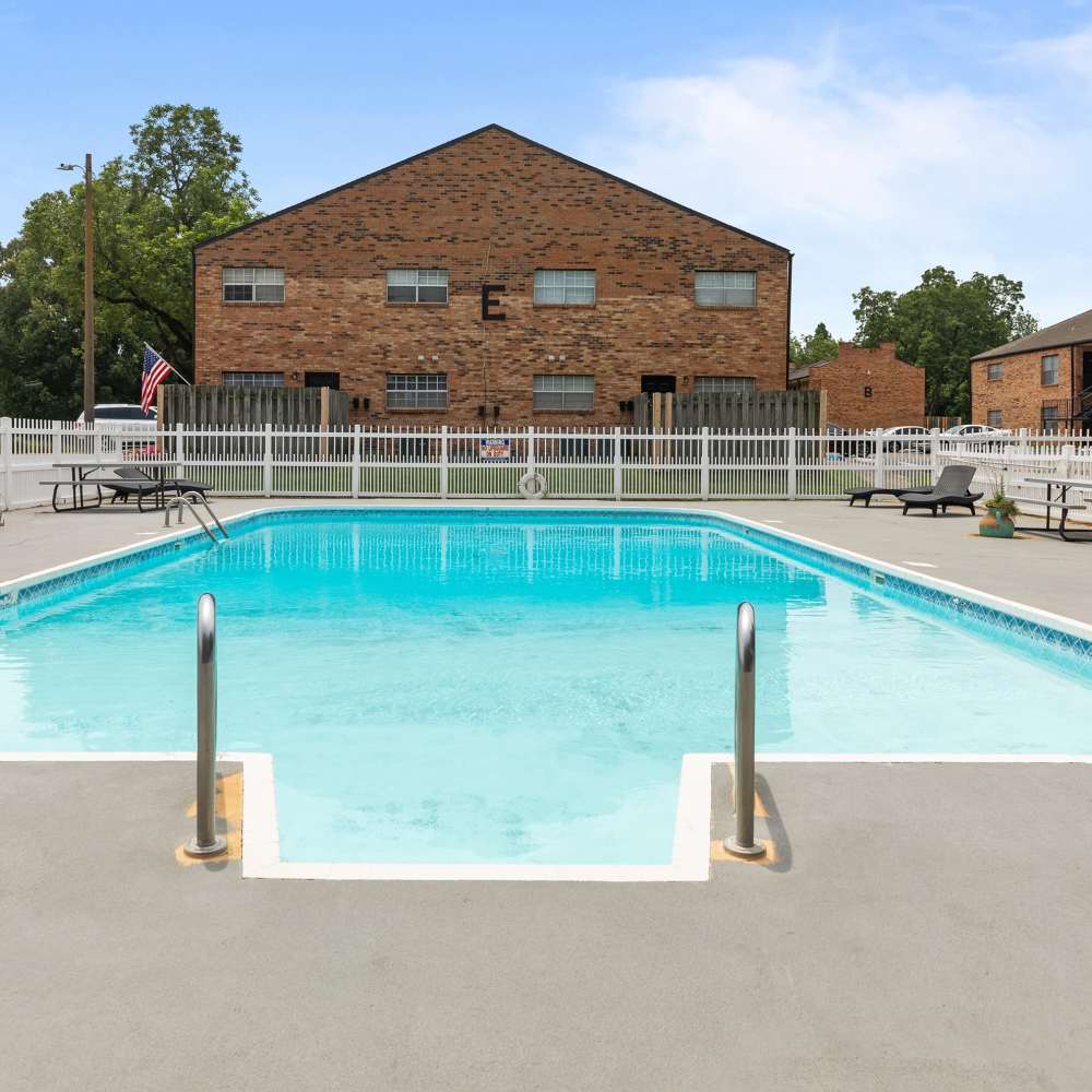 Sparkling water pool surrounded by charming brick apartment buildings and inviting lounge areas at Pecan Ridge in Vicksburg, Mississippi.
