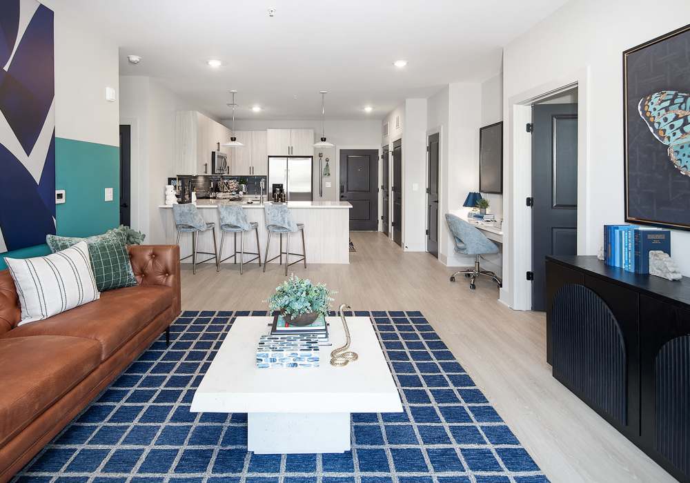 Open-Concept Living Room and Kitchen With Leather Sofa, Coffee Table, Desk Nook, Light Wood Flooring, and Island Seating at Cypress Point in Mooresville, North Carolina.