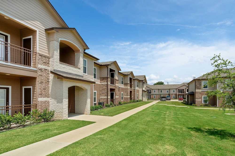 Exterior shot of apartments with lush green walking path at Pine Creek in Paris, Texas