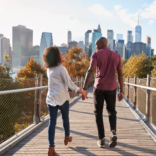 Couple holding hands while they walk across a bridge through the park near Eastgold NYC in New York, New York