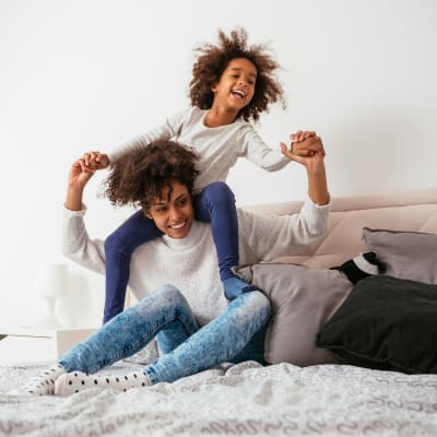 Mother and daughter jumping on bed in a well-lit bedroom at Coral Sea Park in Lemoore, California