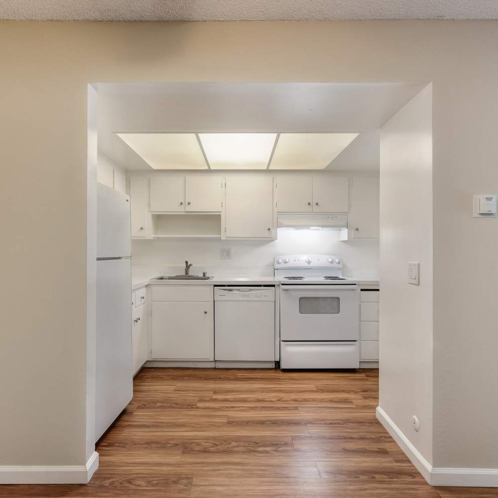 Kitchen with white appliances and cabinetry and living/dining room at Fayette Arms Apartments in Mountain View, California